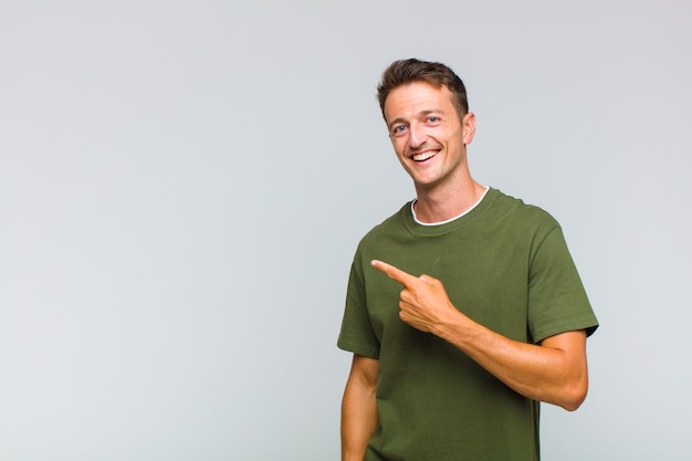 Young handsome man looking excited and surprised pointing to the side and upwards to copy space