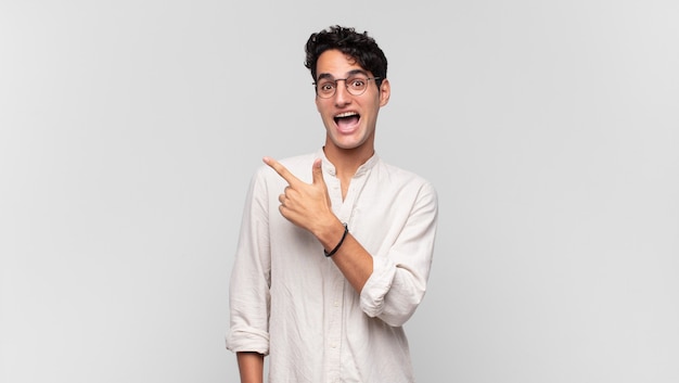 Young handsome man looking excited and surprised pointing to the side and upwards to copy space