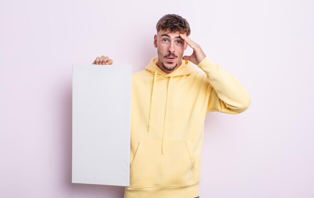 Young handsome man looking happy, astonished and surprised. blank canvas concept