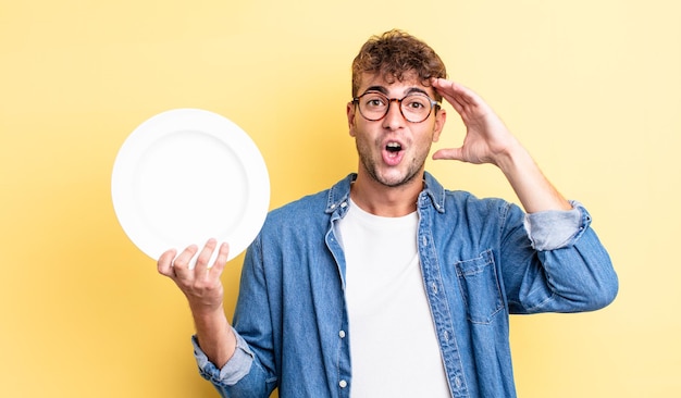 Young handsome man looking happy, astonished and surprised. empty dish concept