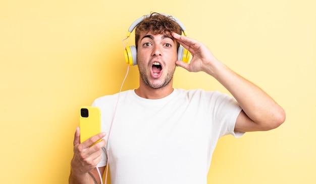 Young handsome man looking happy, astonished and surprised. headphones and smartphone concept