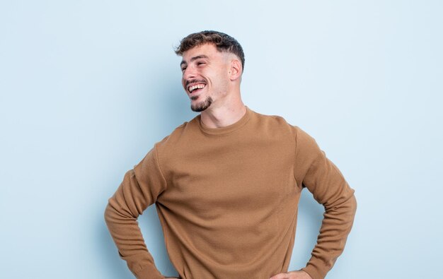 Young handsome man looking happy, cheerful and confident, smiling proudly and looking to side with both hands on hips