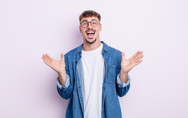 Young handsome man looking happy and excited, shocked with an unexpected surprise with both hands open next to face