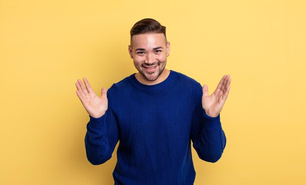 Young handsome man looking happy and excited, shocked with an unexpected surprise with both hands open next to face