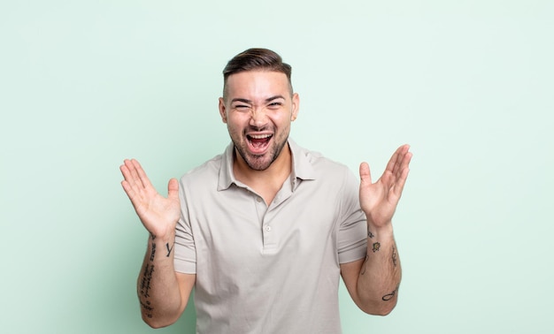 Young handsome man looking happy and excited, shocked with an unexpected surprise with both hands open next to face