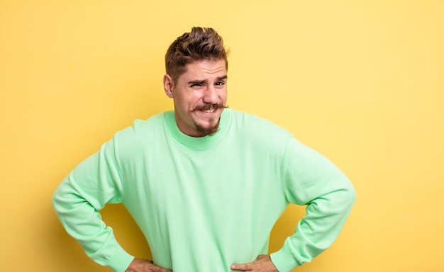 Young handsome man looking happy and friendly, smiling and winking an eye at you with a positive attitude. strange moustache concept