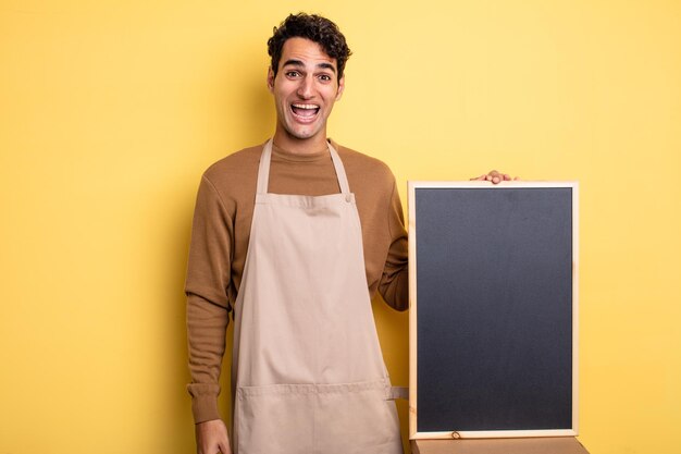 Young handsome man looking happy and pleasantly surprised. chef and blackboard concept