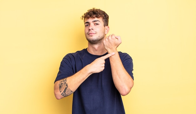 Young handsome man looking impatient and angry, pointing at watch, asking for punctuality, wants to be on time