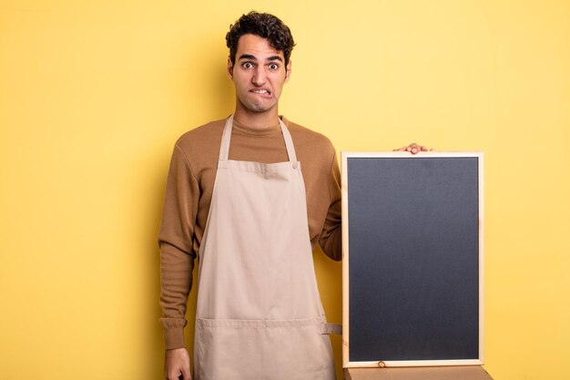 Young handsome man looking puzzled and confused. chef and blackboard concept