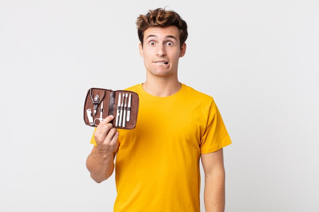 Young handsome man looking puzzled and confused and holding a nails tools case
