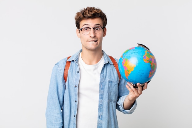 Foto giovane uomo bello che sembra perplesso e confuso. studente con in mano una mappa del globo