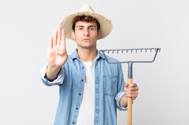 Young handsome man looking serious showing open palm making
stop gesture. farmer concept