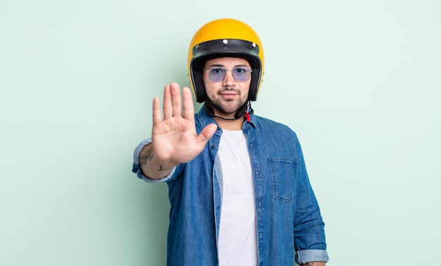 young handsome man looking serious showing open palm making stop gesture. motorbike helmet concept