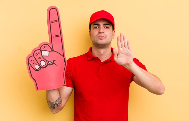 Young handsome man looking serious showing open palm making stop gesture number one hand concept