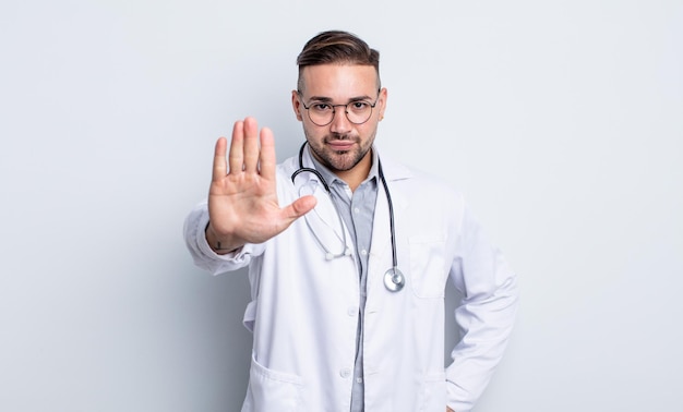 Young handsome man looking serious showing open palm making stop gesture. physician concept