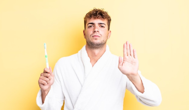 Young handsome man looking serious showing open palm making stop gesture. toothbrush concept