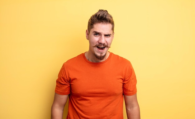 Young handsome man looking shocked, angry, annoyed or disappointed, open mouthed and furious. strange moustache concept