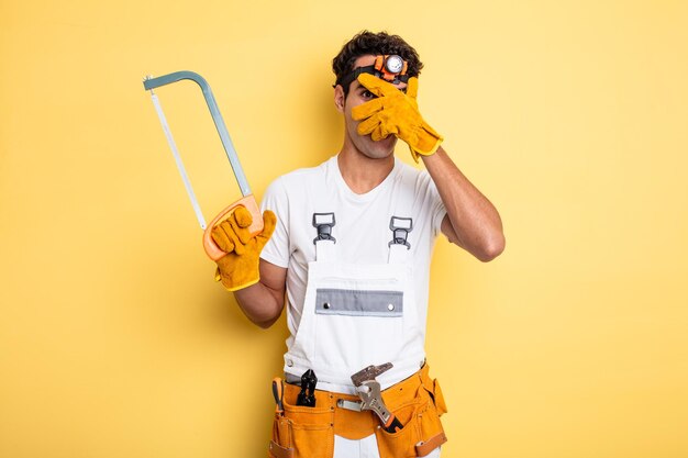 Young handsome man looking shocked, scared or terrified, covering face with hand. handyman repair concept