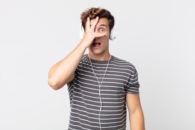 Young handsome man looking shocked, scared or terrified, covering face with hand. listening music concept