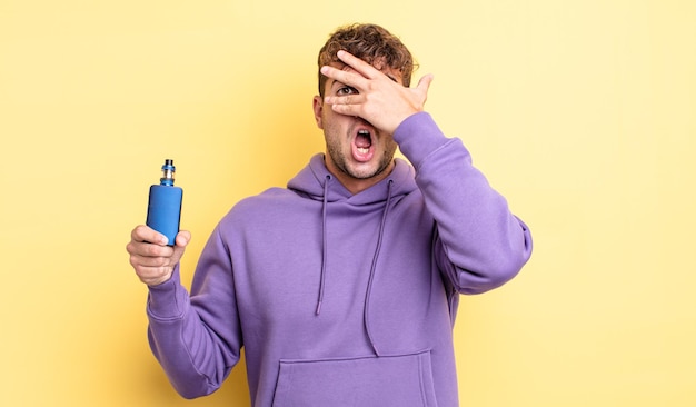 Young handsome man looking shocked, scared or terrified, covering face with hand. vaporizer concept
