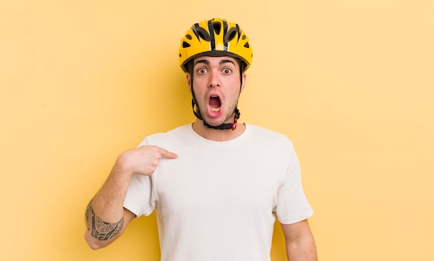 Young handsome man looking shocked and surprised with mouth wide open pointing to self bike concept