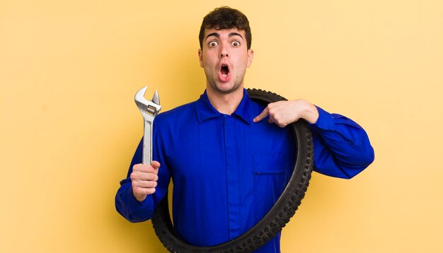 Photo young handsome man looking shocked and surprised with mouth wide open pointing to self bike repairman concept