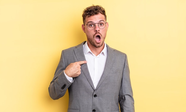 Young handsome man looking shocked and surprised with mouth wide open, pointing to self. business concept