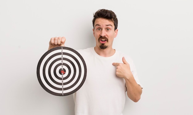 Young handsome man looking shocked and surprised with mouth wide open pointing to self dart target concept