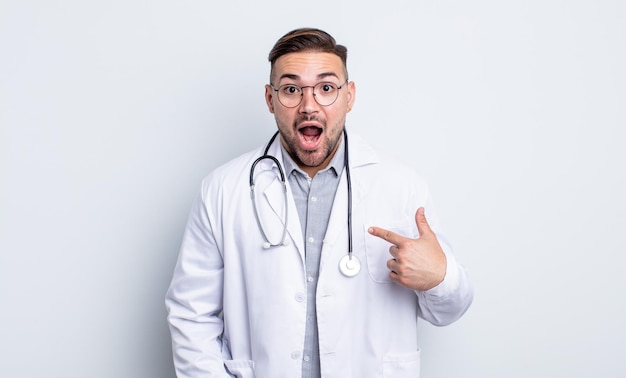 Young handsome man looking shocked and surprised with mouth wide open, pointing to self. physician concept