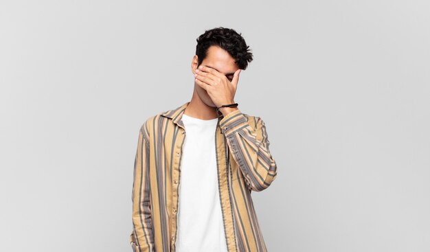 Young handsome man looking stressed, ashamed or upset, with a headache, covering face with hand