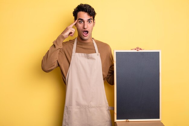 Young handsome man looking surprised, realizing a new thought, idea or concept. chef and blackboard concept