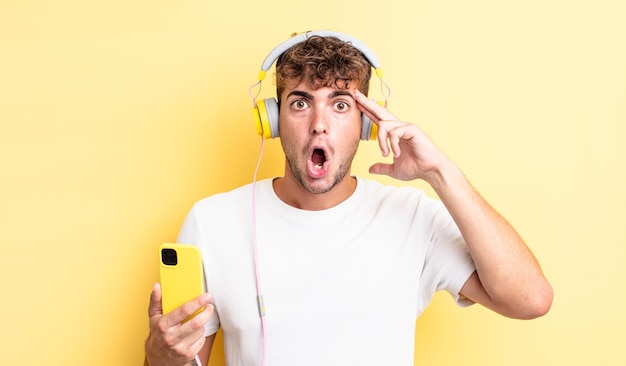 Young handsome man looking surprised, realizing a new thought, idea or concept. headphones and smartphone concept