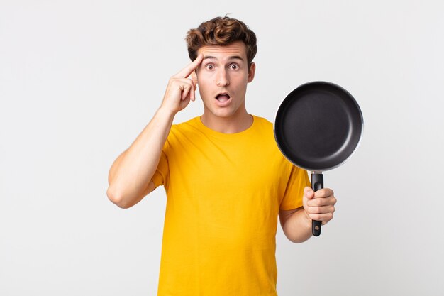 Young handsome man looking surprised, realizing a new thought, idea or concept and holding a cook pan