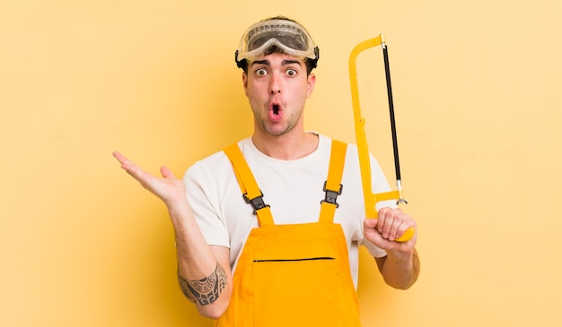 Young handsome man looking surprised and shocked with jaw dropped holding an object handyman concept