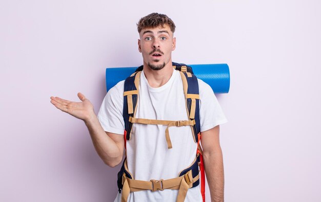 Young handsome man looking surprised and shocked, with jaw dropped holding an object. hiker concept