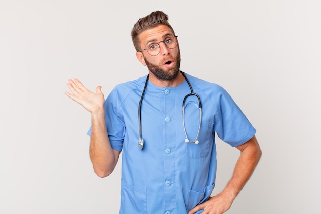 Young handsome man looking surprised and shocked, with jaw dropped holding an object. nurse concept