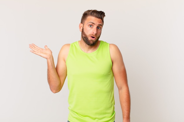 Young handsome man looking surprised and shocked, with jaw dropped holding an object