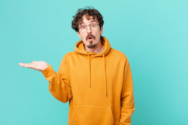 Young handsome man looking surprised and shocked, with jaw dropped holding an object