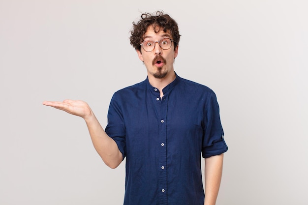 Young handsome man looking surprised and shocked, with jaw dropped holding an object