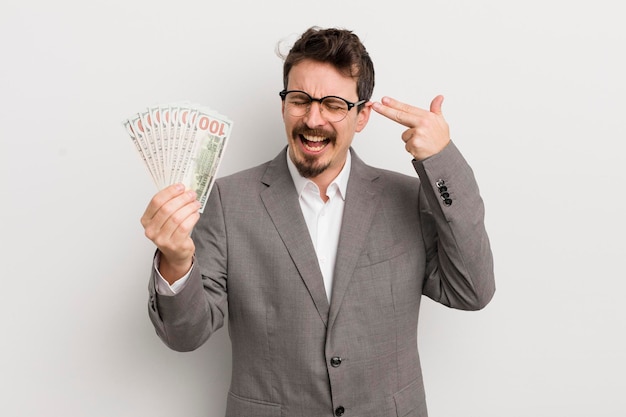 Young handsome man looking unhappy and stressed suicide gesture making gun sign businessman and banknotes