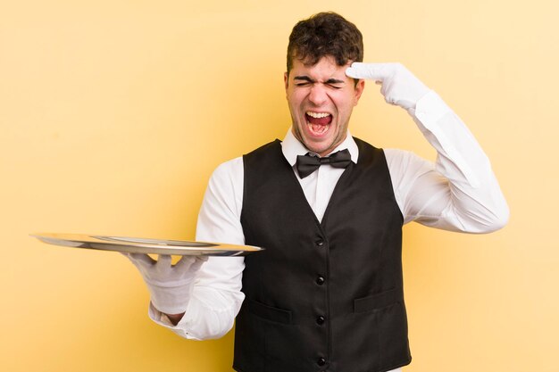 Young handsome man looking unhappy and stressed suicide gesture making gun sign waiter and tray concept