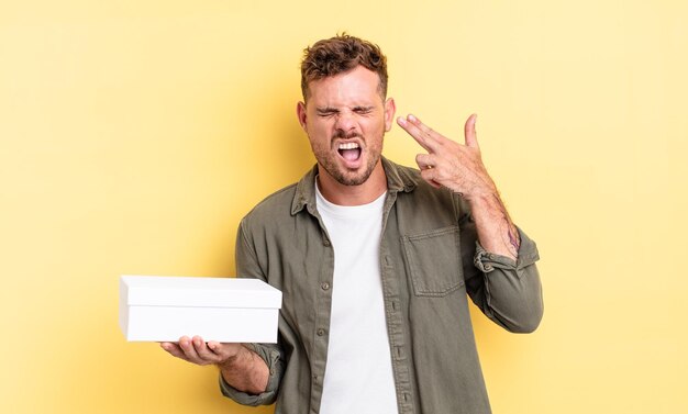 Young handsome man looking unhappy and stressed, suicide gesture making gun sign. white box concept