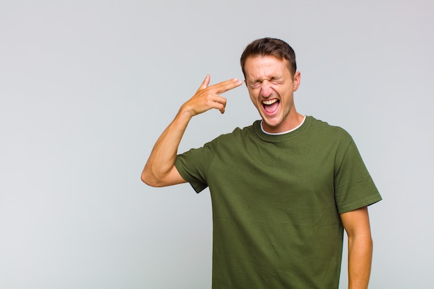 Young handsome man looking unhappy and stressed, suicide gesture making gun sign with hand, pointing to head