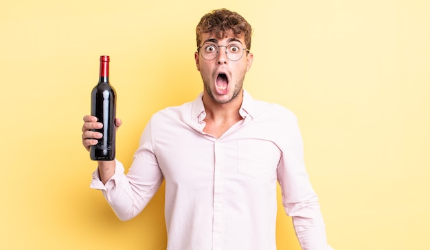 Young handsome man looking very shocked or surprised. wine bottle concept