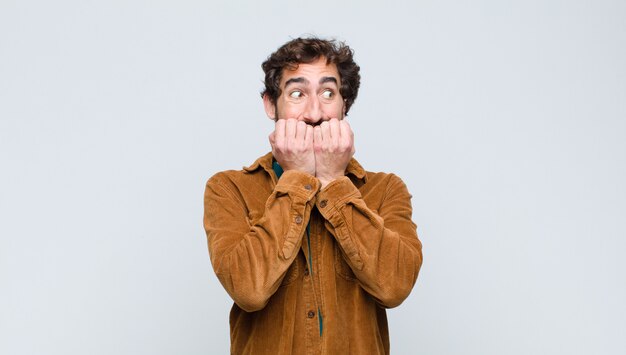 Young handsome man looking worried, anxious, stressed and afraid, biting fingernails and looking to lateral copy space on flat wall