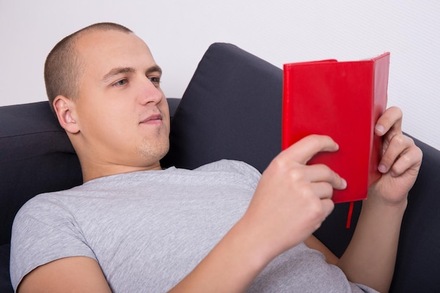 Young handsome man lying on sofa and reading book at home
