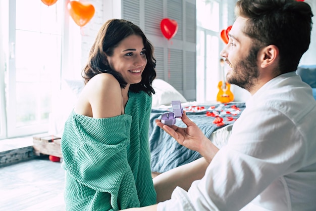 Young handsome man makes a proposal to his beautiful girlfriend to marry him in a beautiful bedroom with a romantic background. Husband and wife