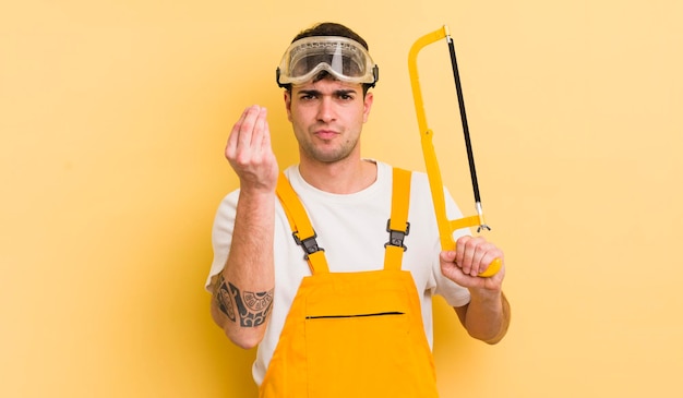 Young handsome man making capice or money gesture telling you to pay handyman concept