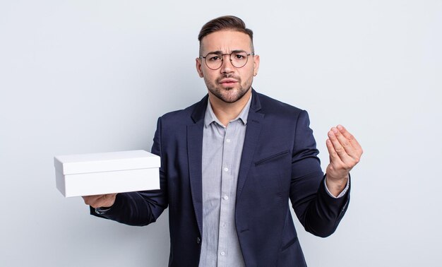 Young handsome man making capice or money gesture, telling you to pay. white box concept