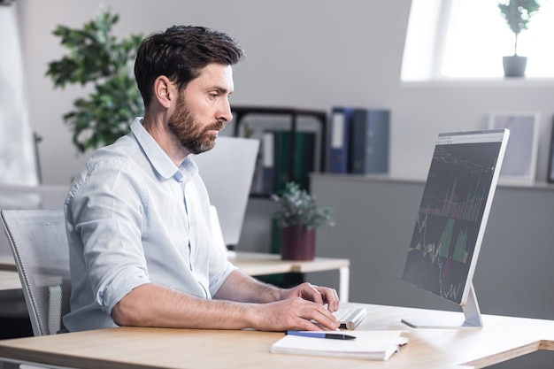 Young handsome man office worker working at a computer with graphics sitting at a table typing on the keyboard explains